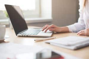 person using a laptop with a pen and notebook by her side