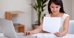 smiling woman looking looking at a paper while using laptop