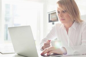 woman using a laptop while holding a mug