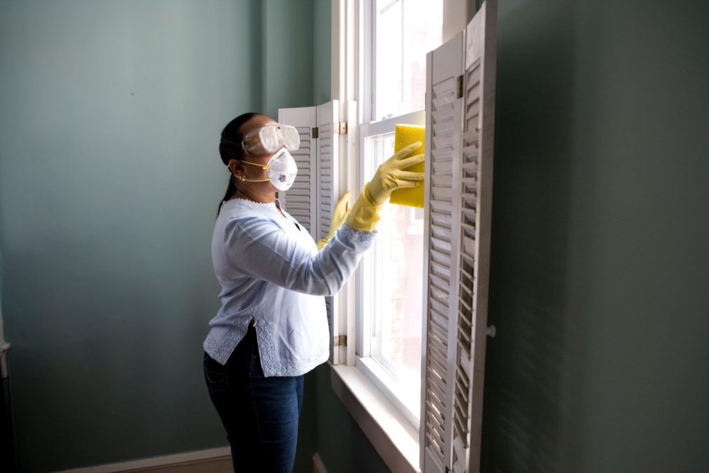 A cleaner with proper protective equipment cleans the windows of a cleaning client's home.